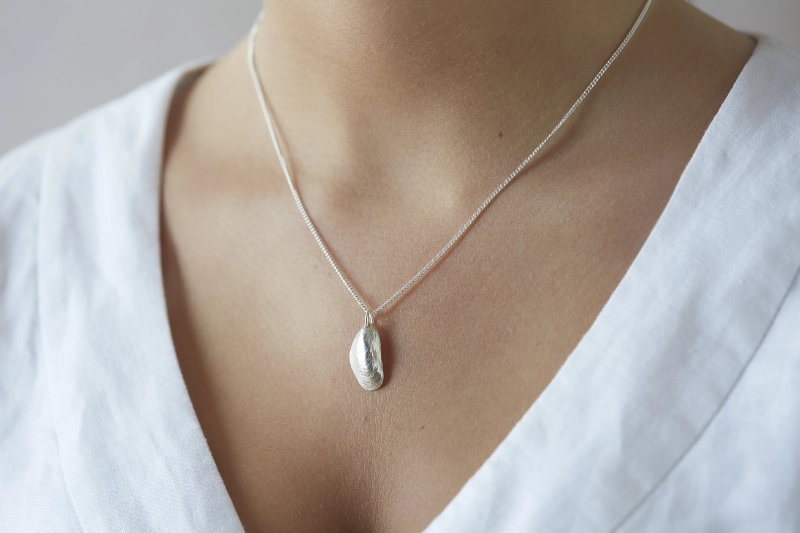 silver mussel shell necklace worn on woman wearing a white linen dress
