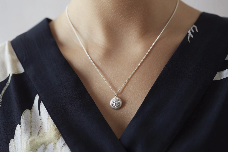 silver bee button necklace worn on woman with black v neck blouse