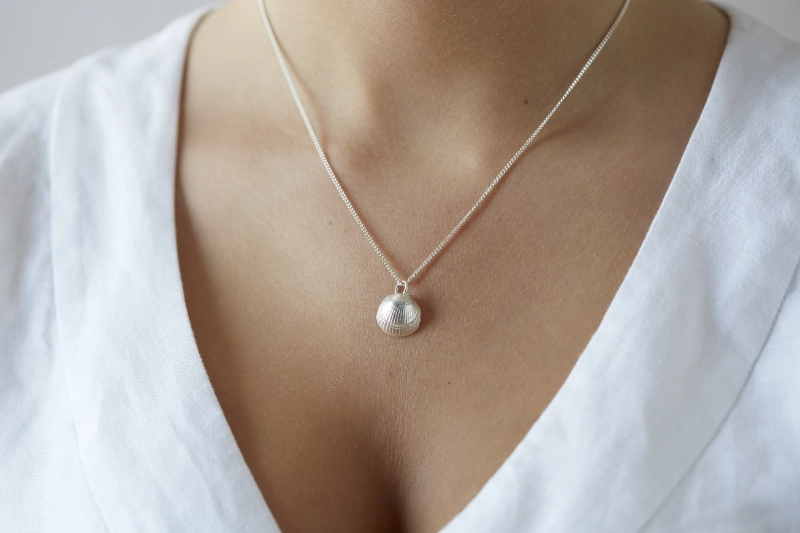 silver cockle shell necklace worn on woman with white linen v neck dress