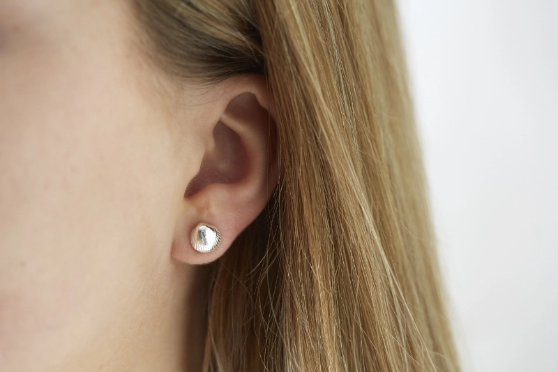 silver cockle shell stud earrings worn in left ear of model with long brown hair