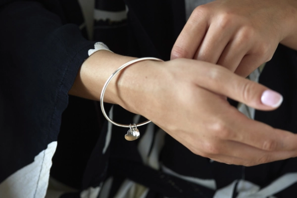 silver bangle with 2 silver curved hearts worn on wrist of model wearing black dress