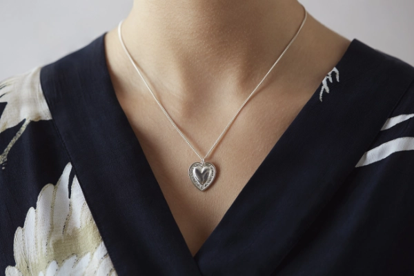 silver heart button necklace worn on woman with v neck black dress