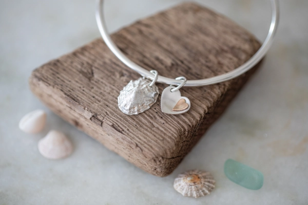 silver limpet shell bangle resting on driftwood and with shells in the foreground