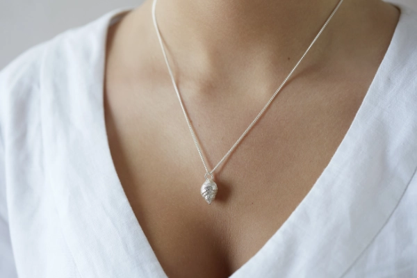 whelk shell necklace worn by model in white v neck linen dress
