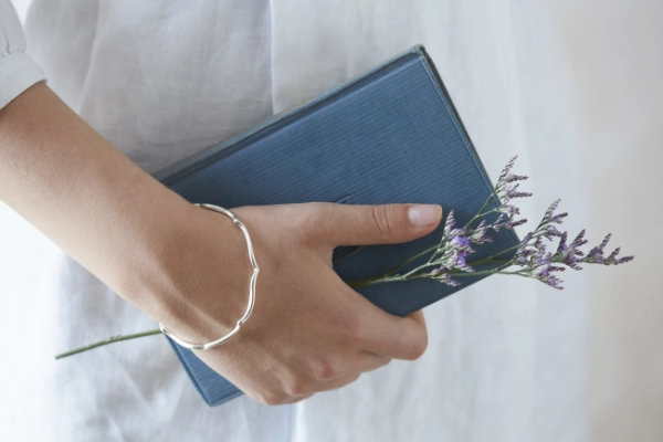 silver wave bangle worn by model on wrist holding spring of lavender and vintage blue book