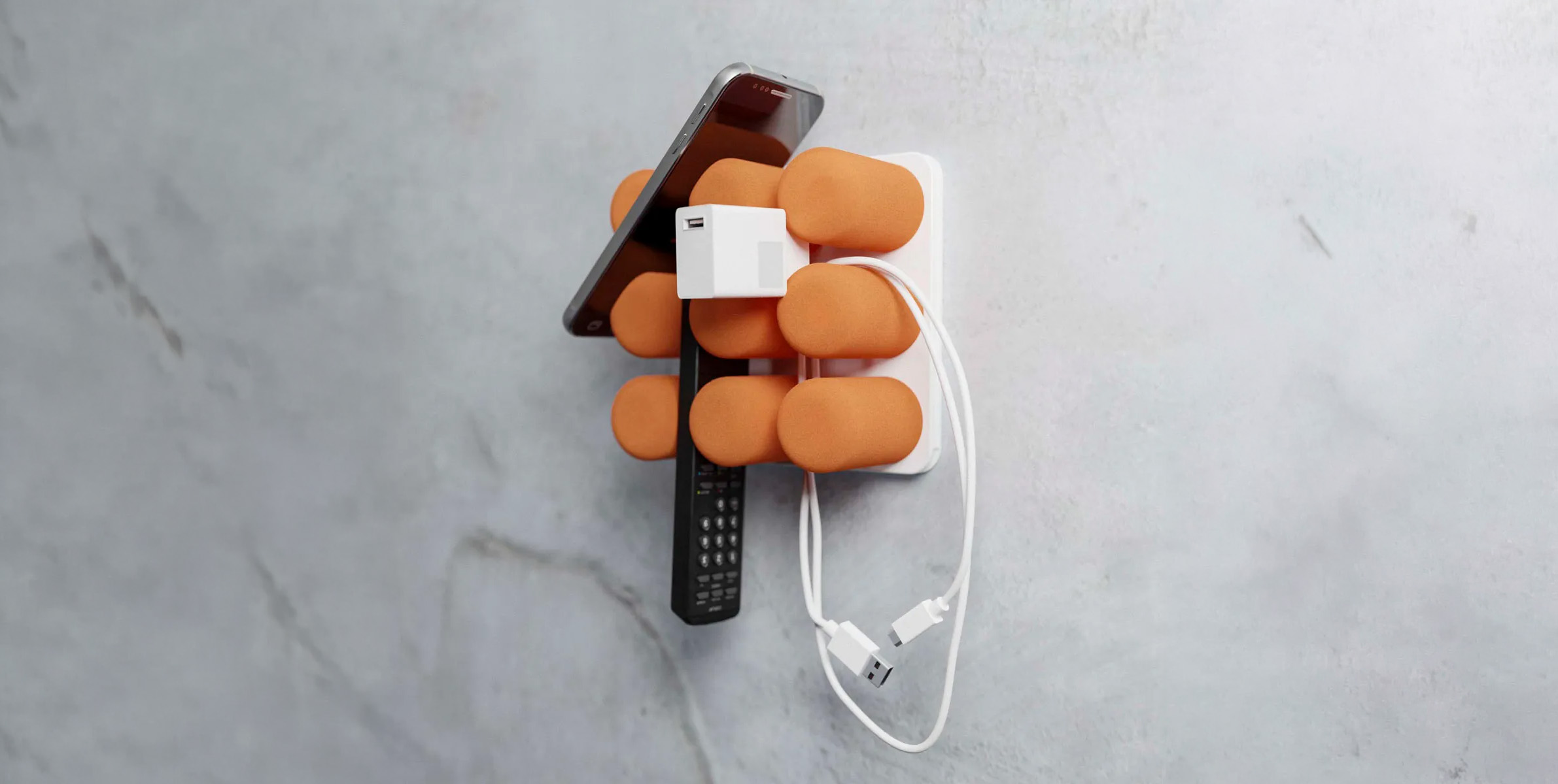 Pinnns Halterung in Orange mit Smartphone und Ladekabel an einer Wand