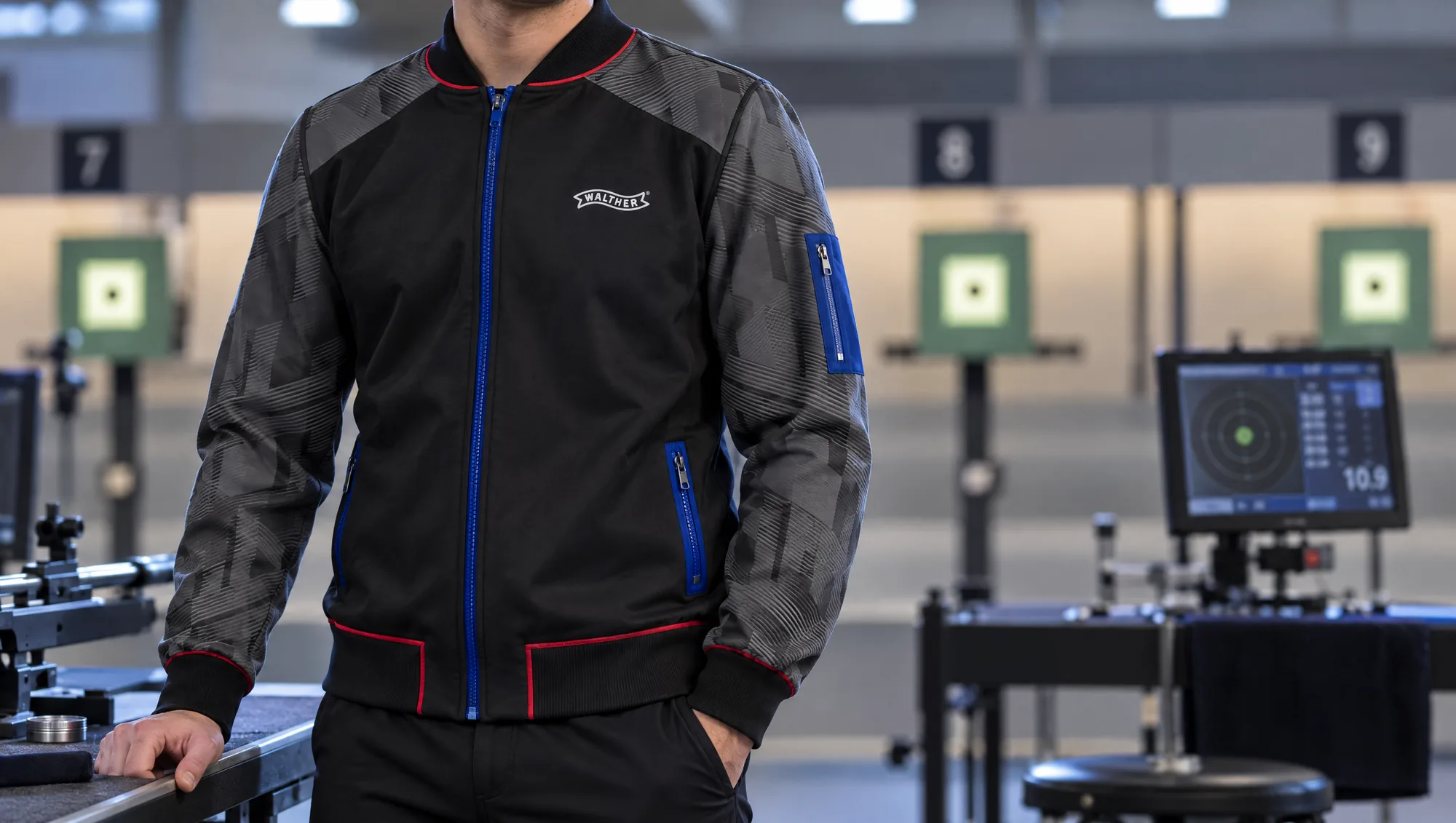 Schwarze Schützenjacke von Carl Walther mit blauem Reißverschluss und roten Paspeln am Schießstand