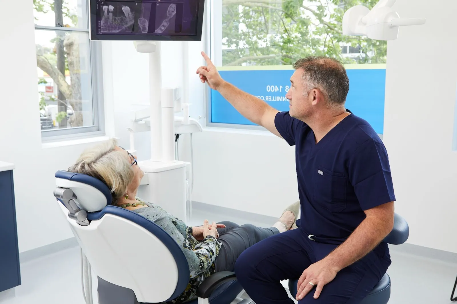 A patient listens to Dr Adamo and looks at scans on a screen in the Dental Implants on Miller clinic in Sydney.