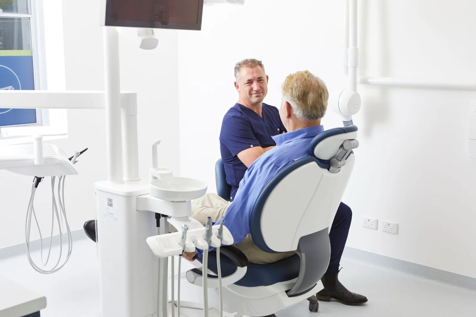 Dr Adamo sits with a patient in his  luxurious, comfortable and state-of-the-art clinic at Dental Implants on Miller in Sydney.