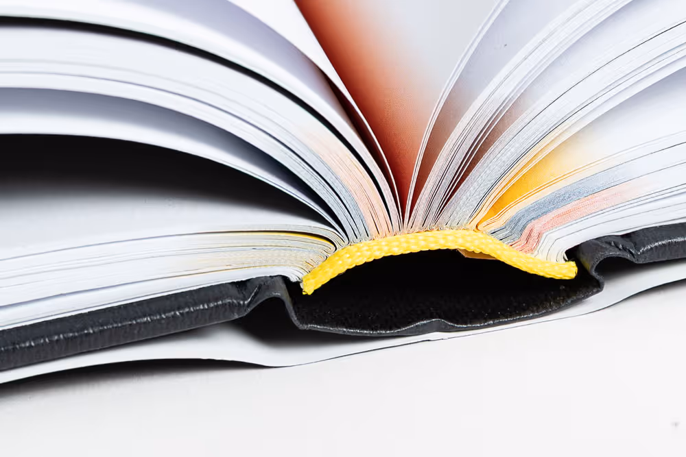 Close-up of an open book showing colorful page edges and a yellow fabric spine detail.