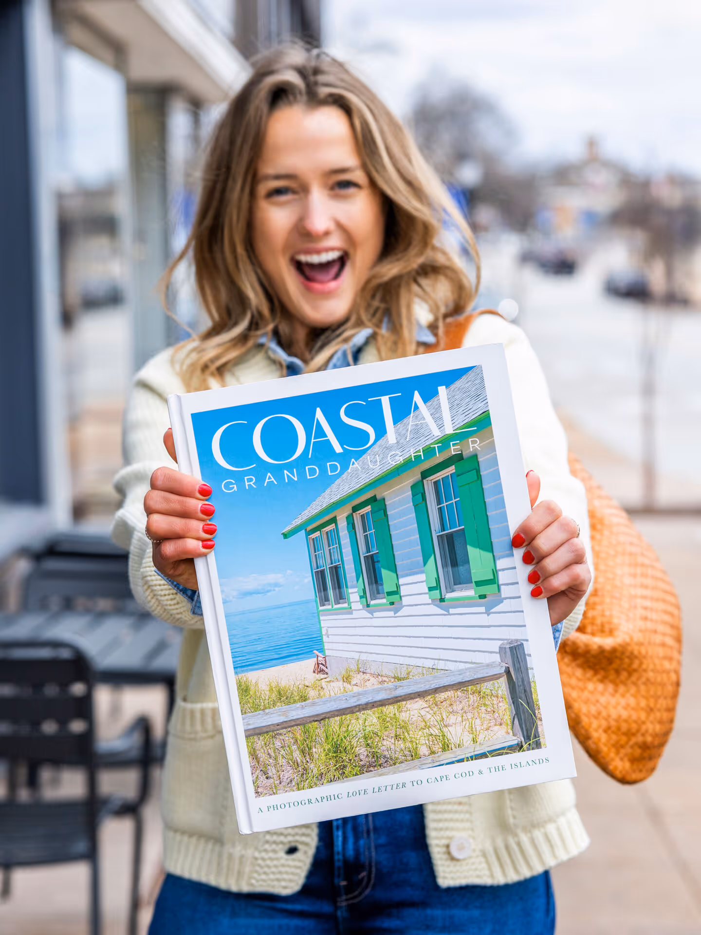 Smiling woman holding the book Coastal Granddaughter with a photo of a beach house on the cover.