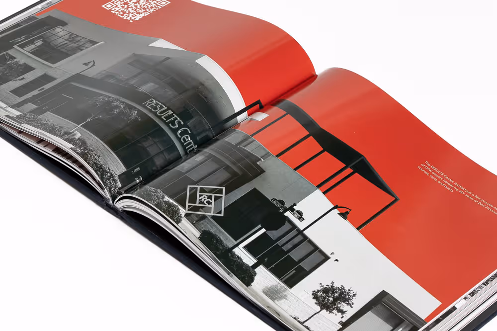 Open coffee table book showing a black and white photo of the RESULTS Center building with a red background on the right page.