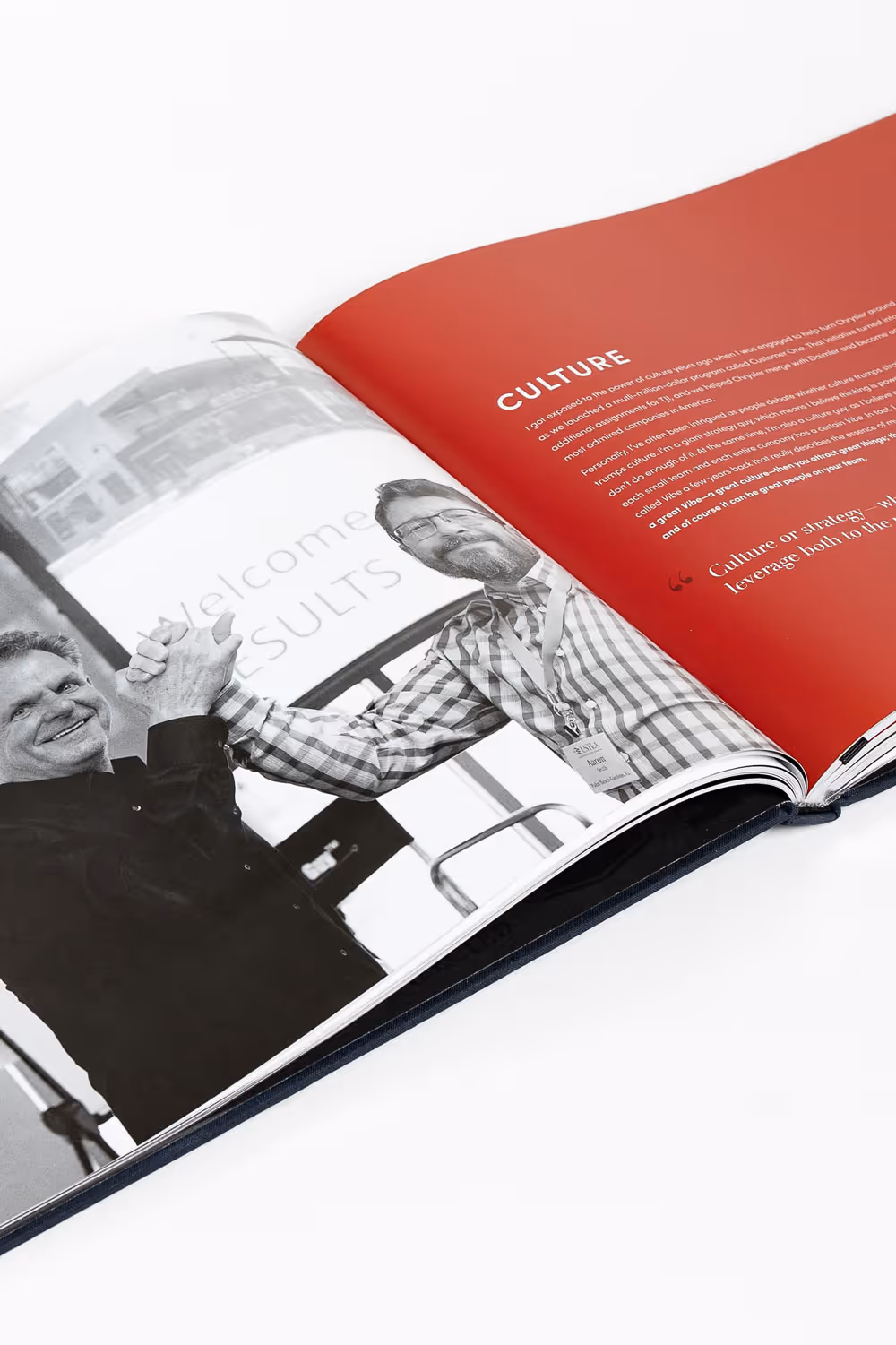 Open coffee table book titled "Results" spread with a black-and-white photo of two men clasping hands and a red page titled 'CULTURE' with text.