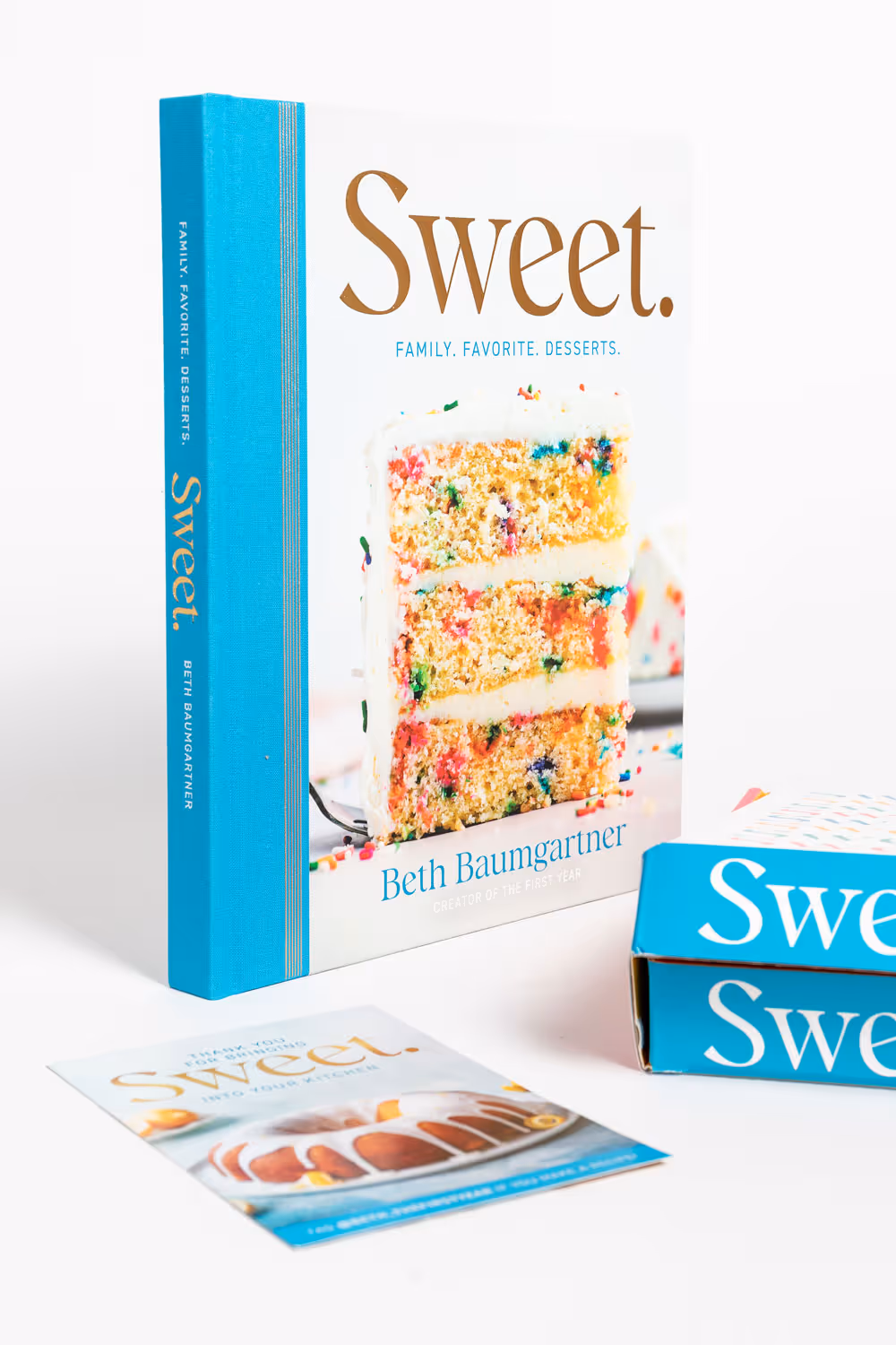Cookbook titled 'Sweet. Family. Favorite. Desserts.' by Beth Baumgartner with a close-up image of a three-layer cake with white frosting and colorful sprinkles on the cover.