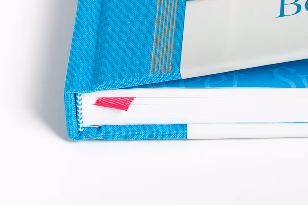 Close-up of a closed blue cookbook, "Sweet" by @beth_thefirstyear with a red bookmark ribbon.