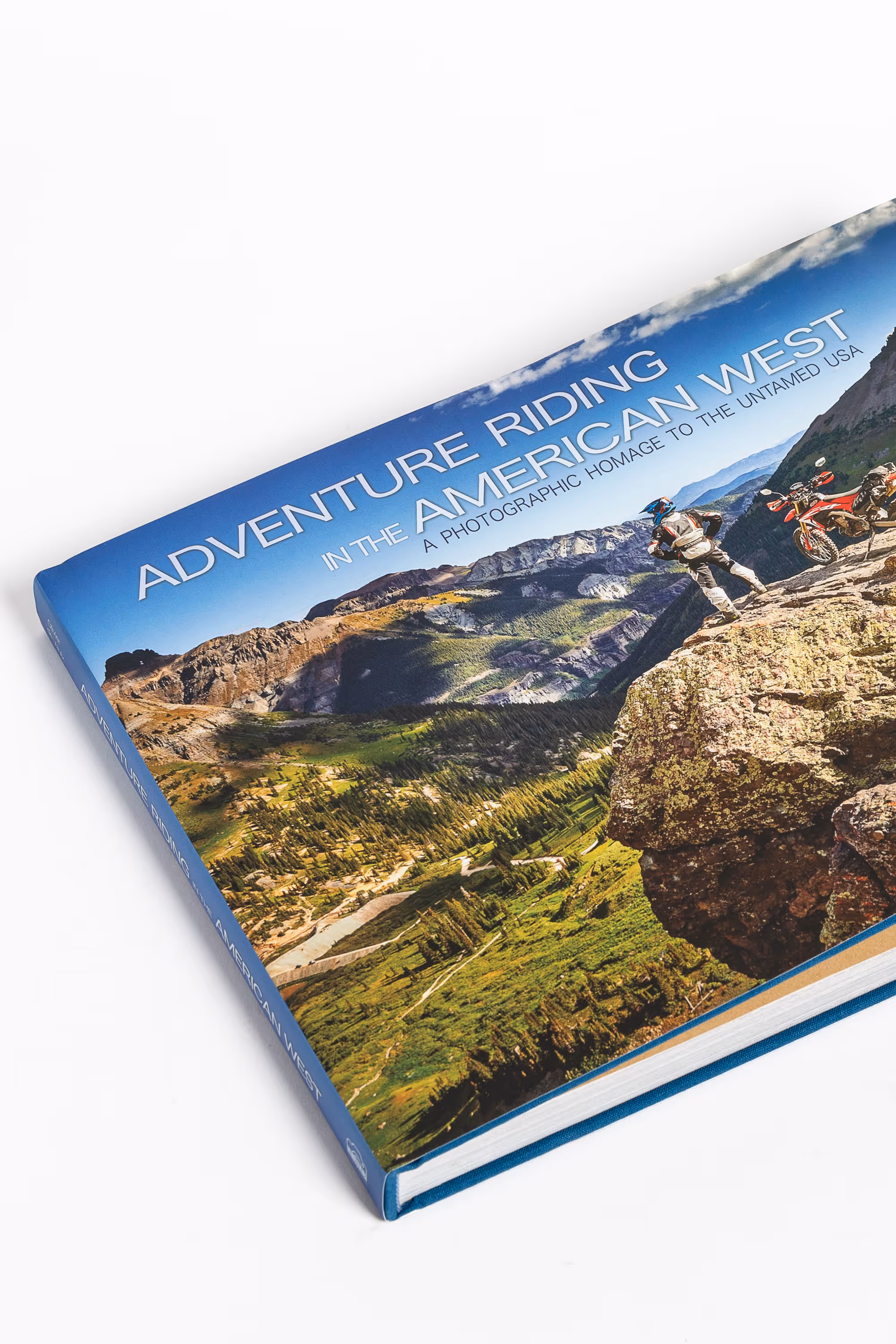 Hardcover book titled 'Adventure Riding in the American West' featuring a mountain landscape with a motorcyclist standing on a rock next to two motorcycles.