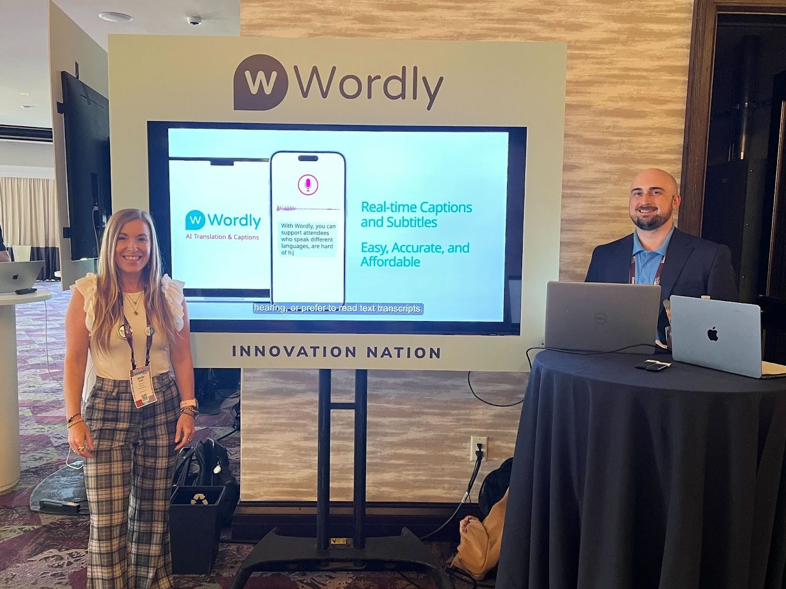 Wordly team members at the PCMA CEMA Summit 2025 Innovation Zone, standing beside a large screen displaying the Wordly AI translation and caption services.
