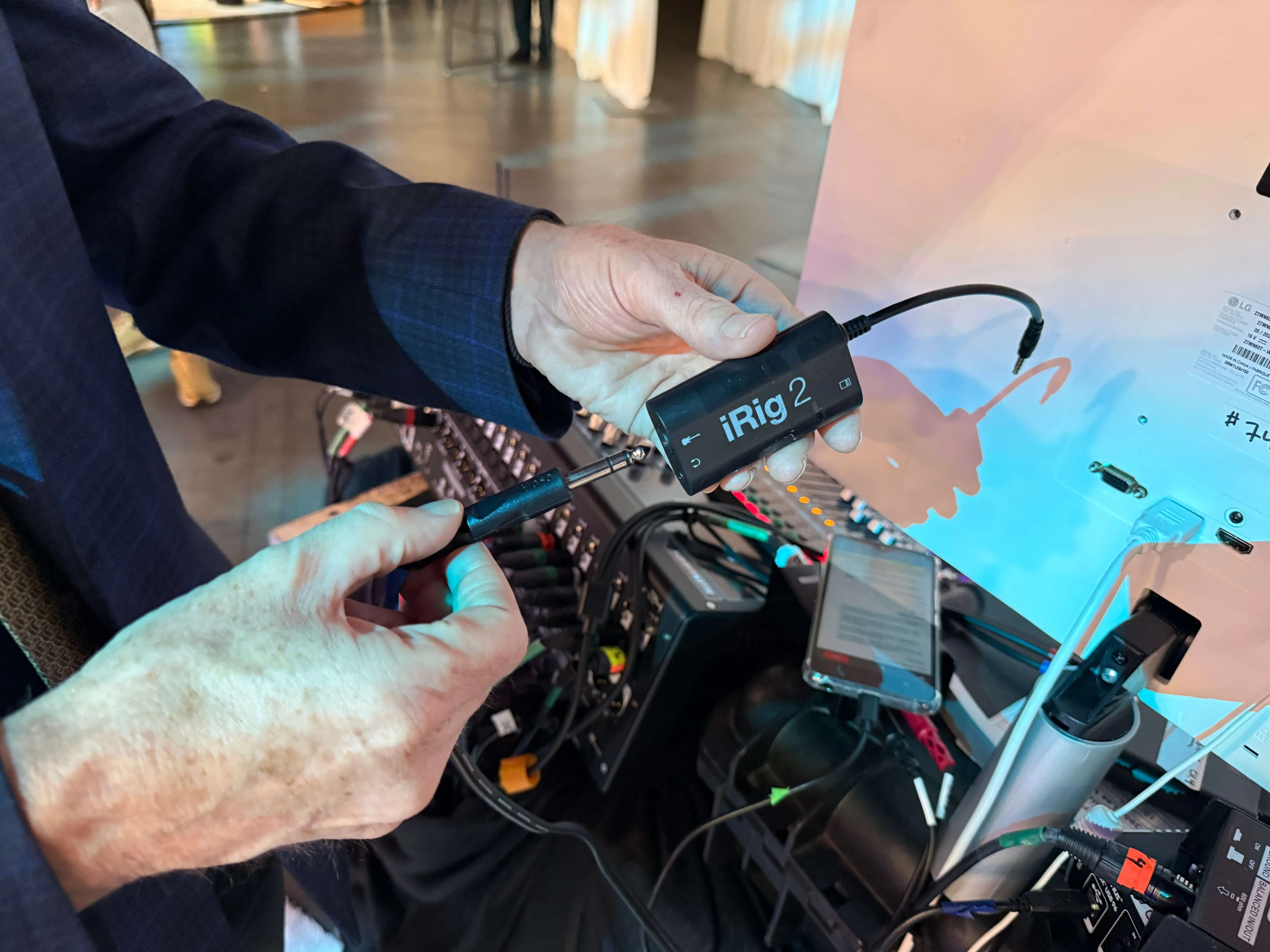 A person holds an iRig 2 audio converter device connected to an audio mixer with multiple cables during an event setup. The iRig is shown as part of a Wordly AV connection.
