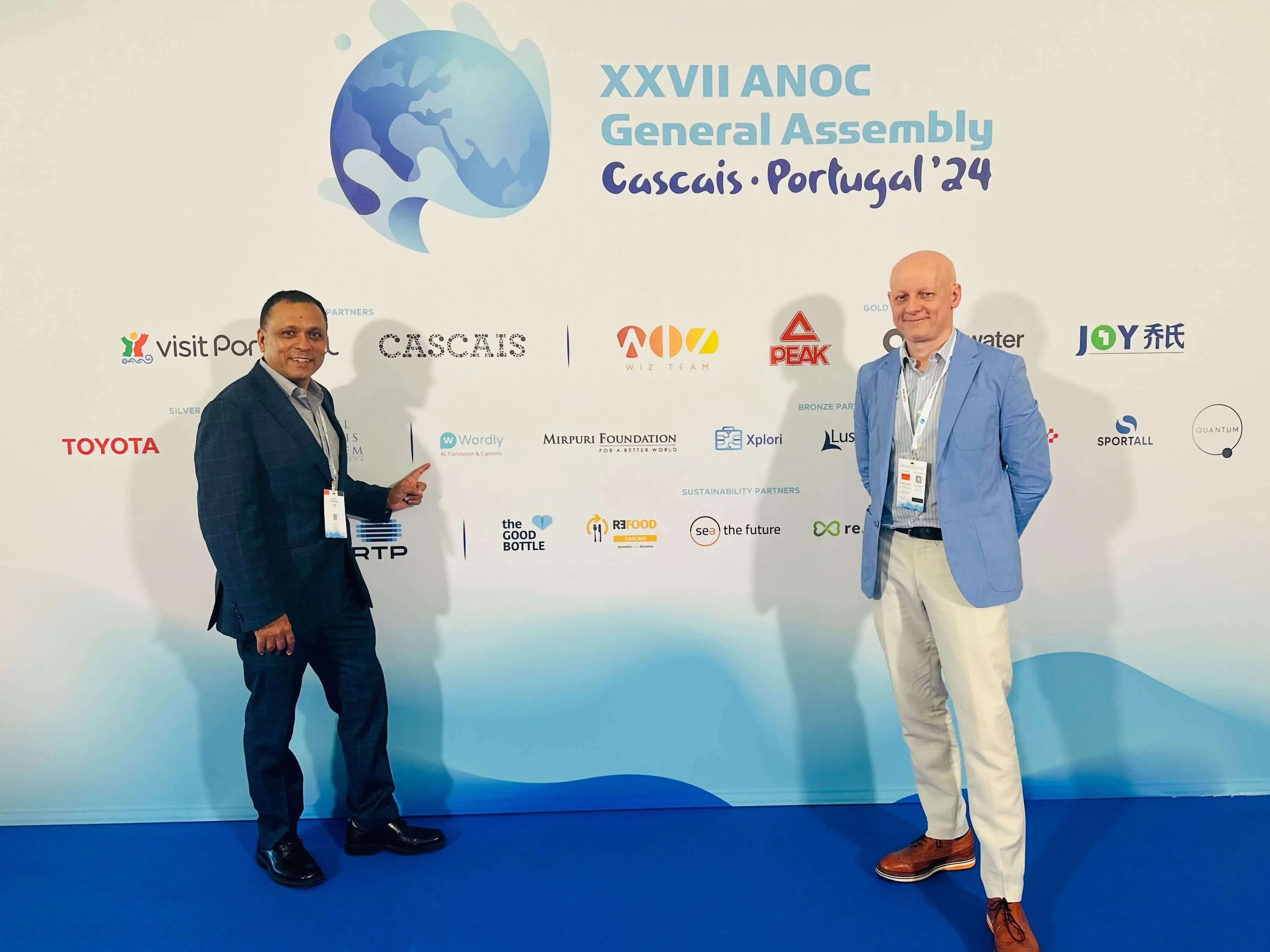 Wordly team stand in front of event backdrop. The backdrop displays logos of event partners and sponsors, including Wordly, Toyota, and Visit Portugal.