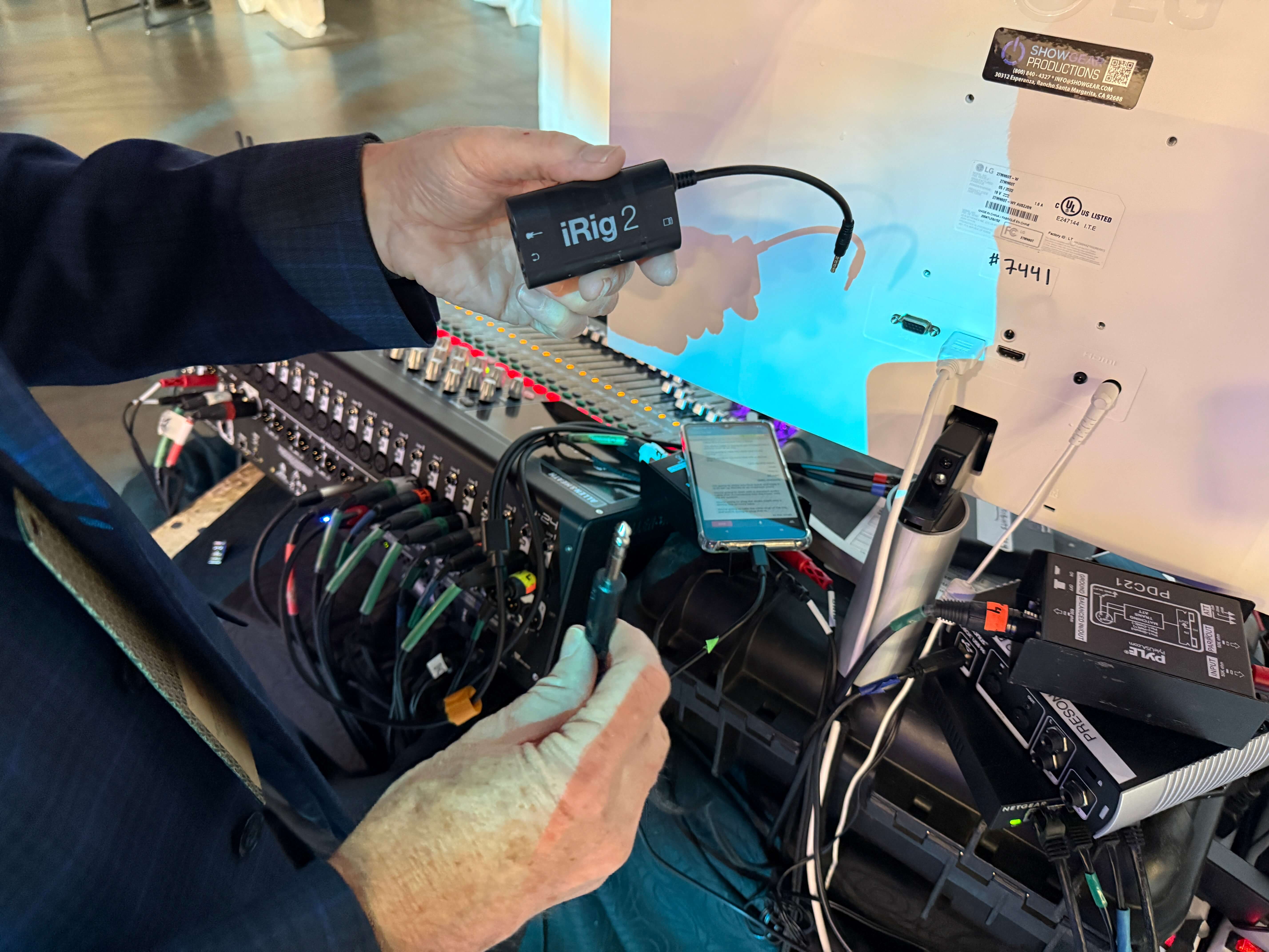 A person holds an iRig 2 audio converter device and an audio mixer during an event setup. The iRig is shown as part of a Wordly AV connection, linking the mixer to a smartphone for real-time audio input to the Wordly AI system.