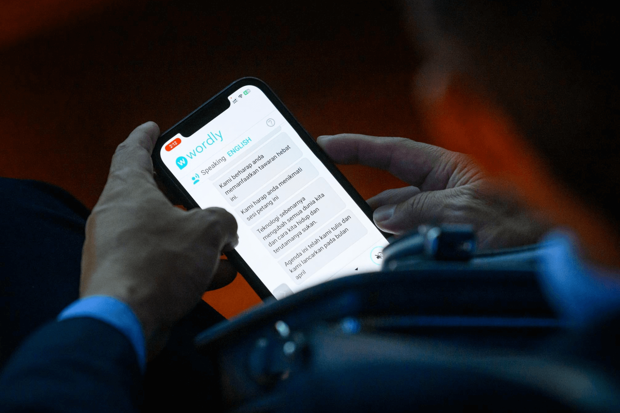 An EAO conference attendee uses Wordly on their smartphone to view real-time AI translation of a live session, displaying English-to-Indonesian subtitles on screen