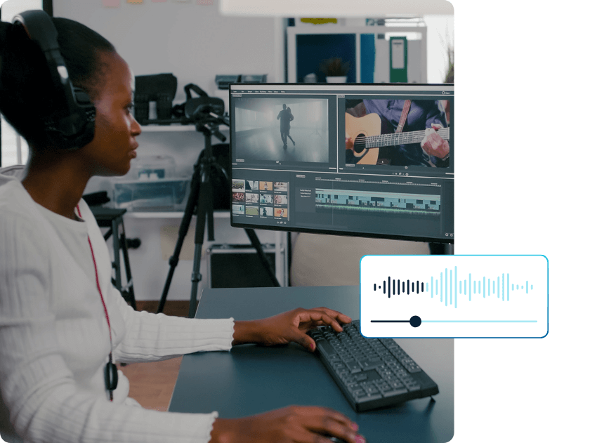 A video editor wearing headphones edits a video on a desktop computer, with an audio waveform graphic symbolizing AI dubbing and Wordly Voice Transcripts.