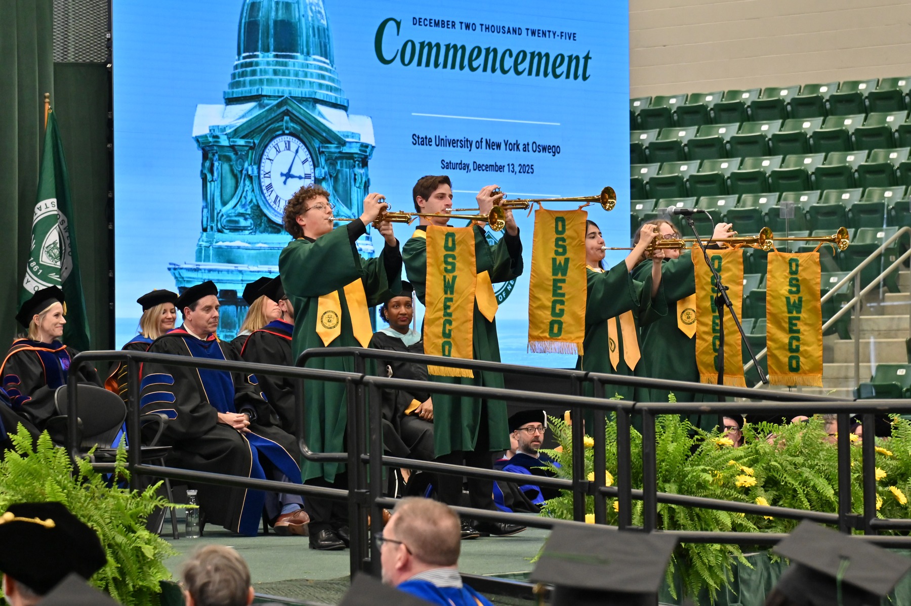 Student trumpeters with gold Oswego banners perform on stage at SUNY Oswego’s Commencement