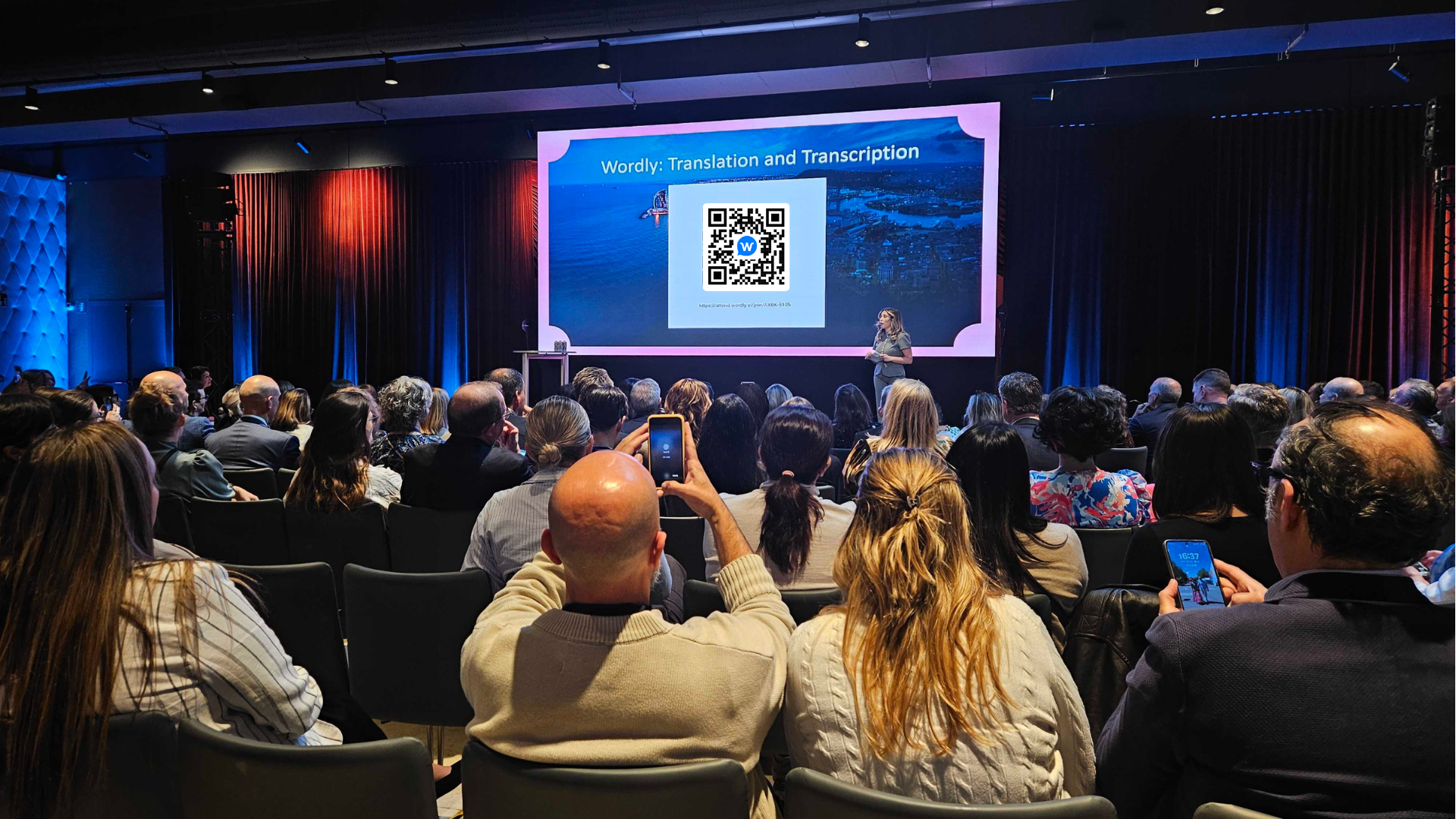 Conference attendees scan a Wordly QR code on the stage screen to access live translation and captions on their phones during a session