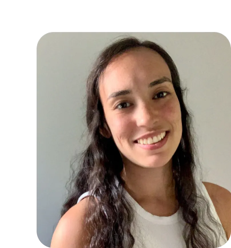 Smiling woman with long curly dark hair wearing a white sleeveless top against a plain gray background.
