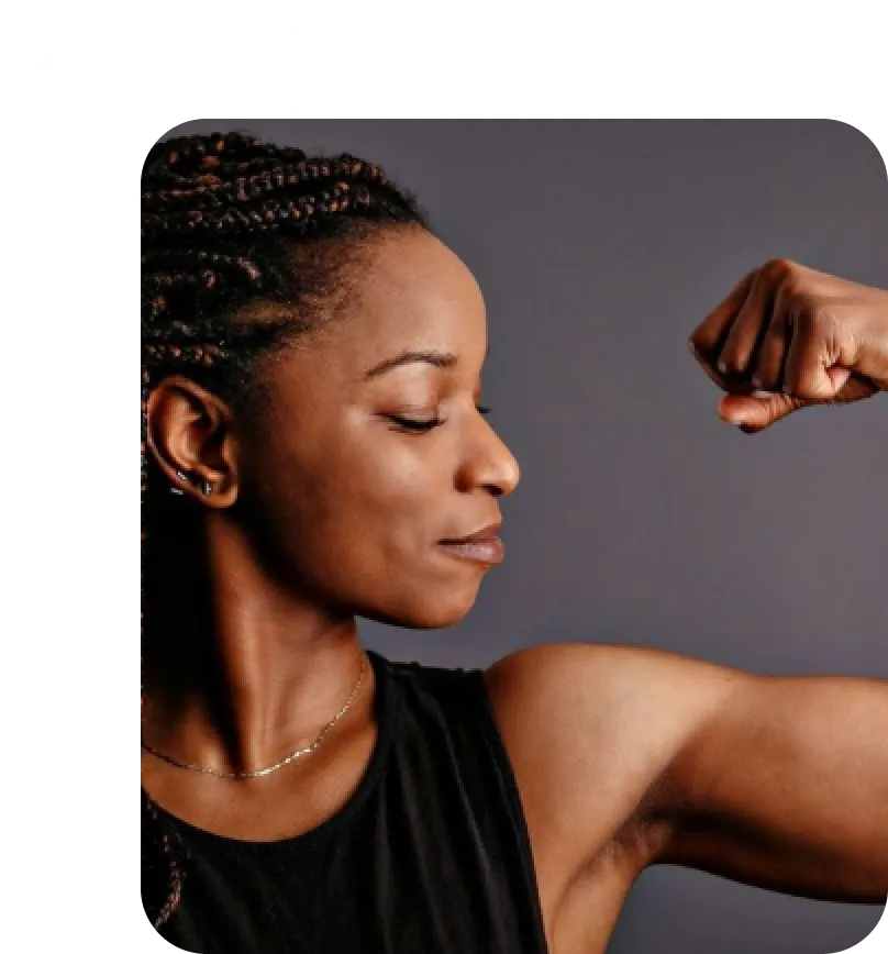 Woman flexing her arm muscle and looking at it with confidence against a plain dark background.