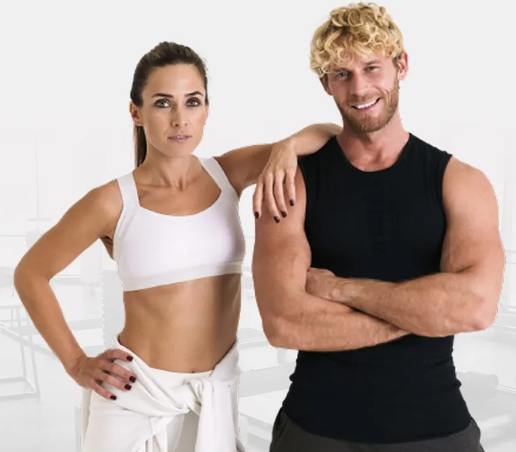 Fit woman in white sportswear and fit man in black sleeveless shirt posing confidently in gym.