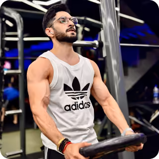 Muscular man in a white Adidas tank top and glasses lifting a weight plate in a gym.