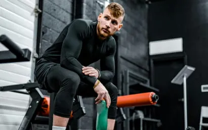Athletic man in black workout clothes sitting on a bench in a gym.