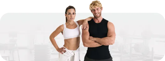 Fit man and woman standing confidently in a gym with exercise equipment in the background.