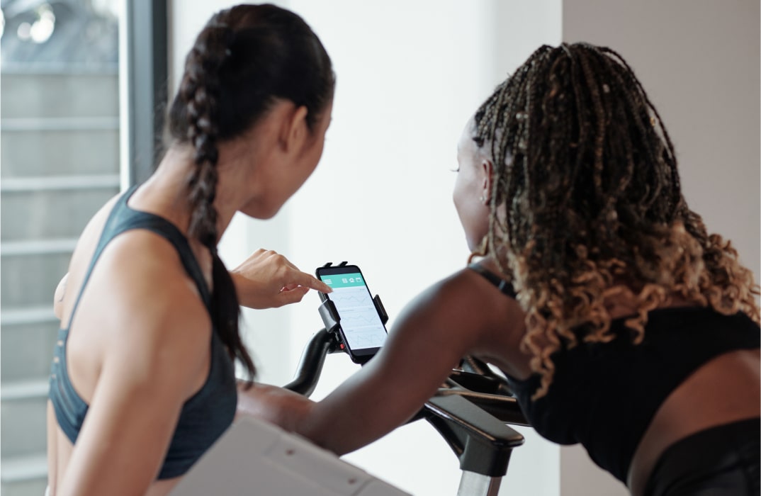Two fitness professionals reviewing app data on a smartphone during a workout, representing real-time performance tracking and user-centric development.