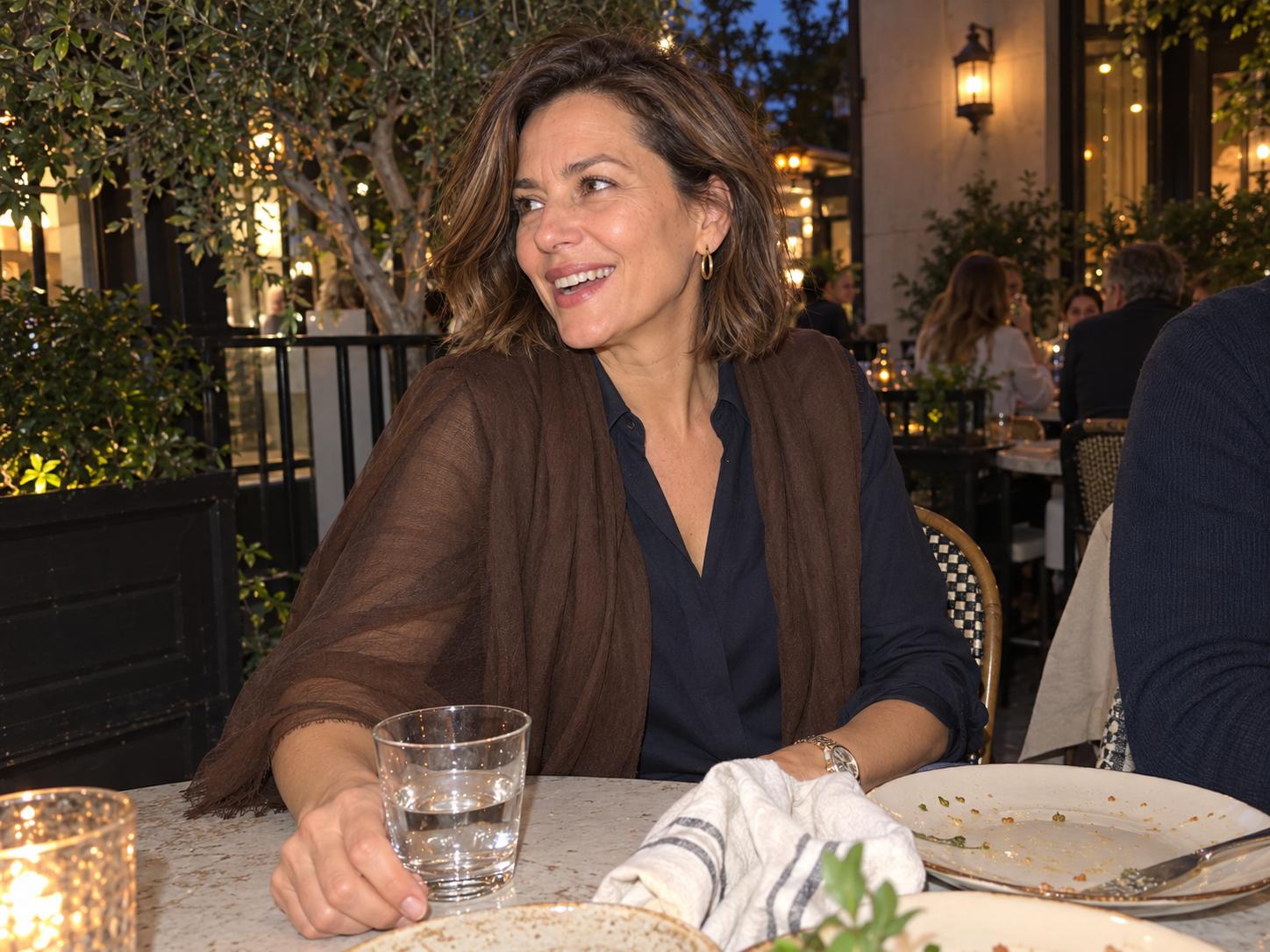 Fashion blogger wearing a Chocolate Featherlight cashmere scarf as a shoulder wrap at an outdoor dinner.