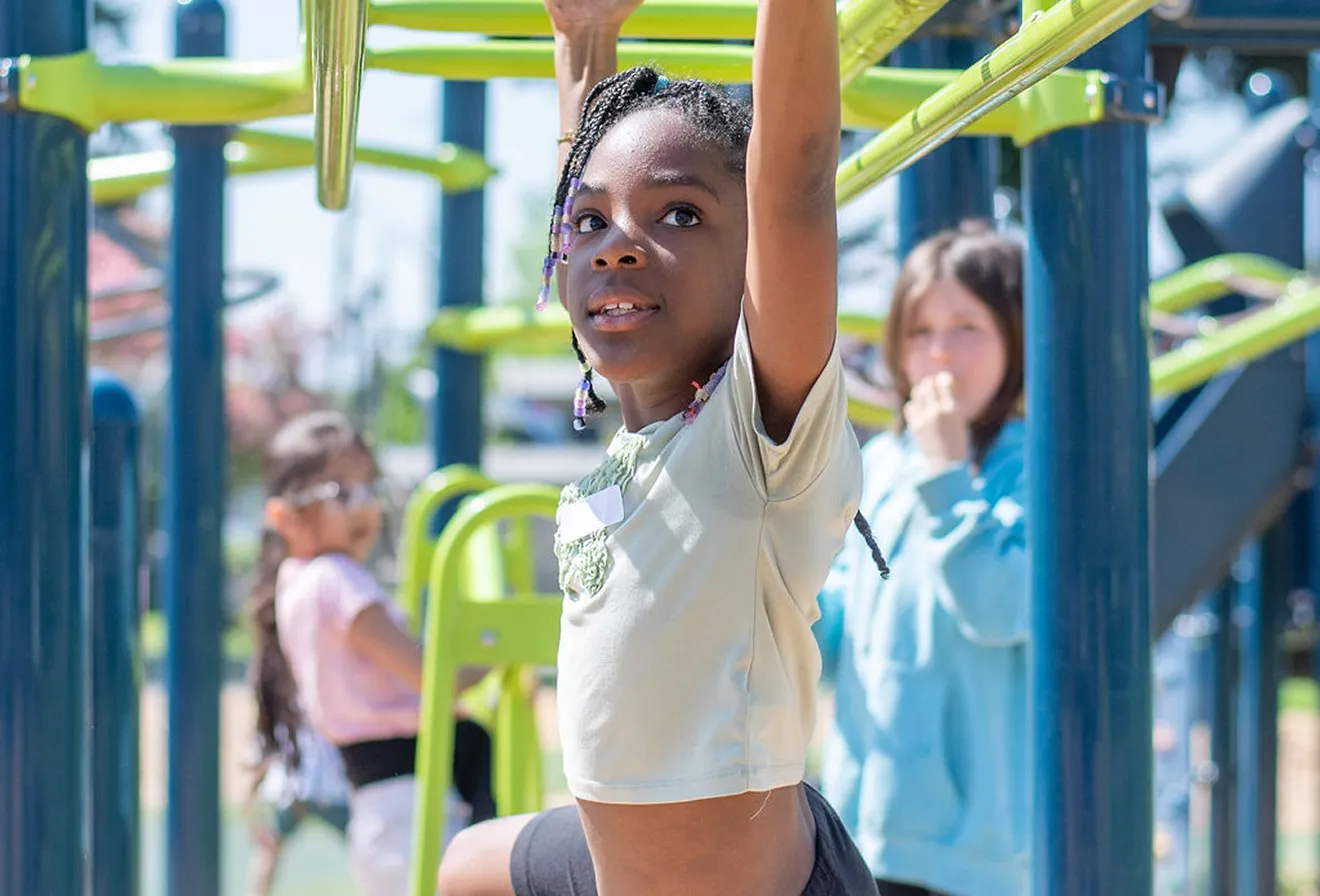 Young girl with braided hair reaching for monkey bars at a colorful outdoor playground.