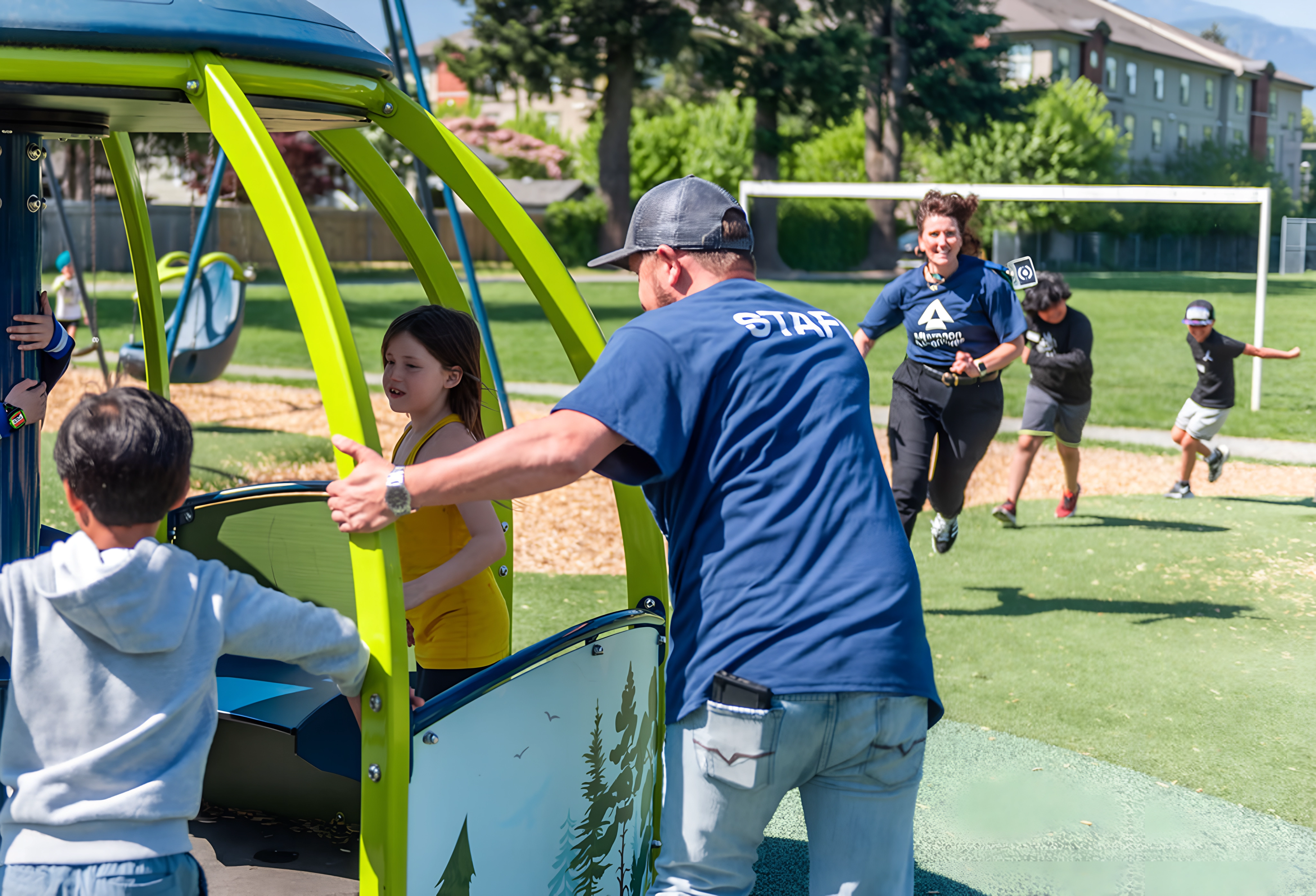 Adults and children play together on a playground merry-go-round on a sunny day.