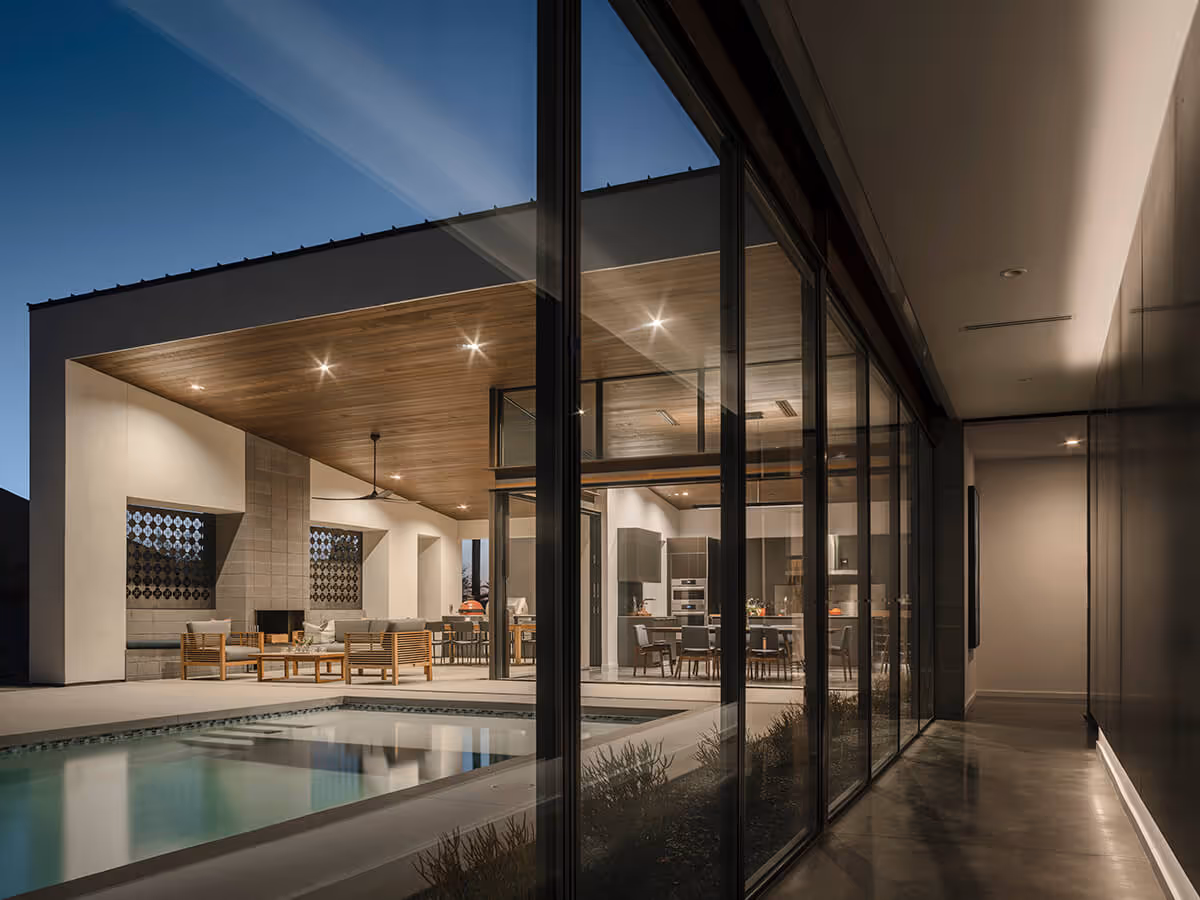 Night view of a glass hallway with a view out to a pool and outdoor living at a modern home in Phoenix by The Ranch Mine