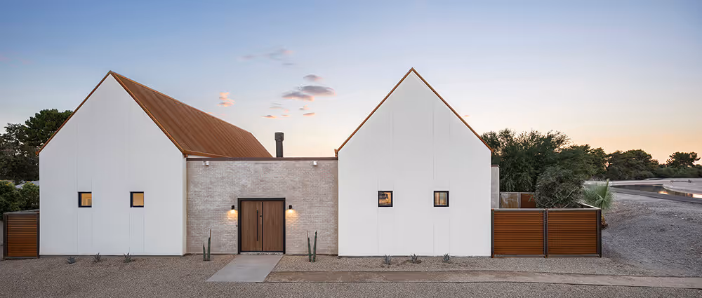 Dusk view of an exterior with white stucco, adobe colored brick and rusted steel at a southwest modern house by The Ranch Mine