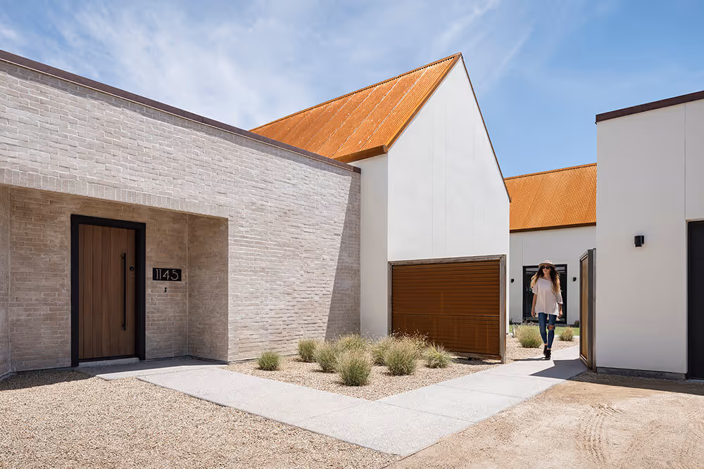 Exterior with white stucco, adobe colored brick and rusted steel at a southwest modern house by The Ranch Mine