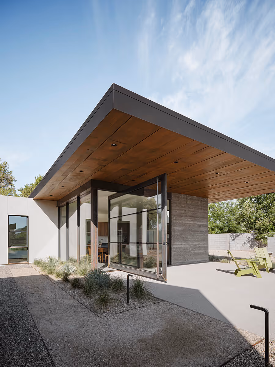 Huge steel and glass pivot door, large cantilevered roof with wood ceiling and boardformed concrete wall and stucco on a casita in Phoenix by The Ranch Mine