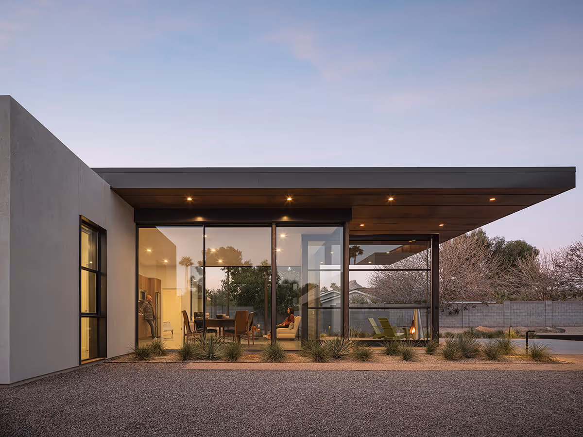 Dusk view of floor to ceiling glass and a large cantilevered roof with wood ceiling on a casita in Phoenix by The Ranch Mine