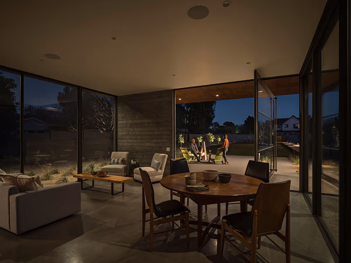 Dusk view of interior of a huge steel and glass pivot door and boardformed concrete wall on a casita in Phoenix by The Ranch Mine