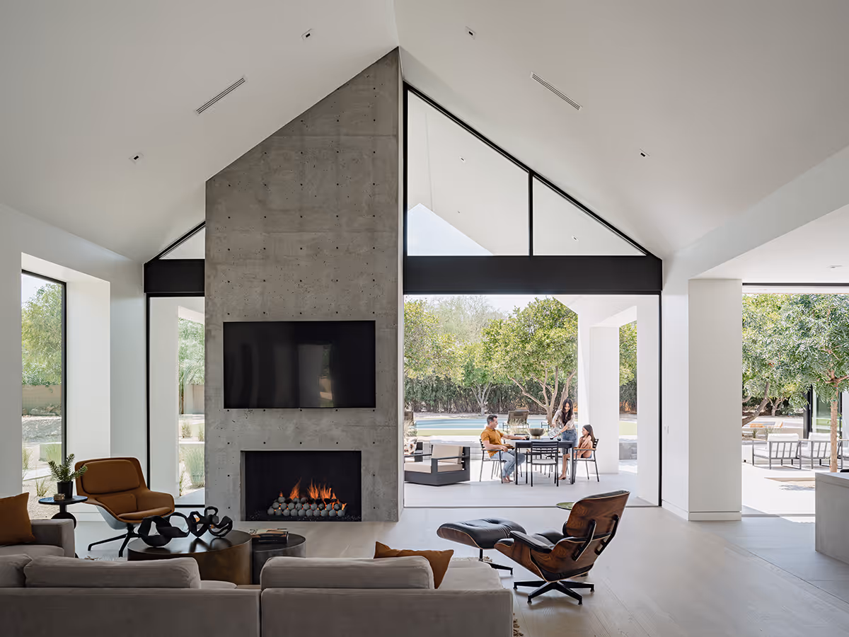 concrete fireplace with indoor outdoor living through pocketing sliding glass doors at modern gable house in Paradise Valley Arizona by The Ranch Mine