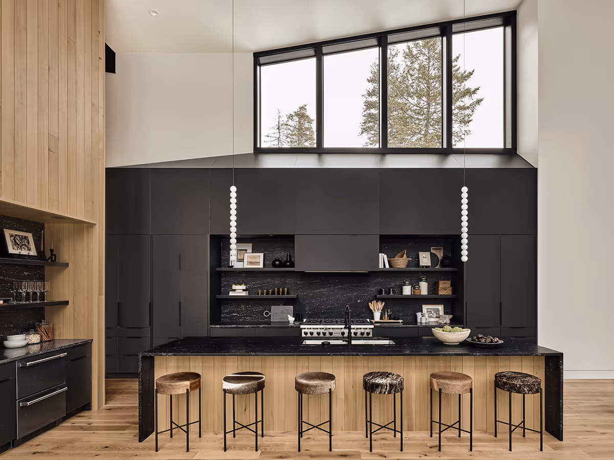 Black kitchen with wood accents and lots of windows looking at a pine forest in Whitefish, Montana