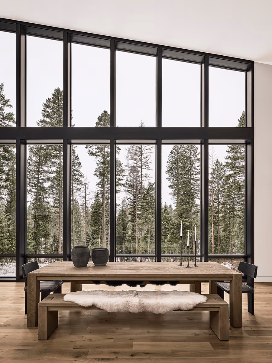 Dining room with a wood table and lots of windows looking at a pine forest in Whitefish, Montana