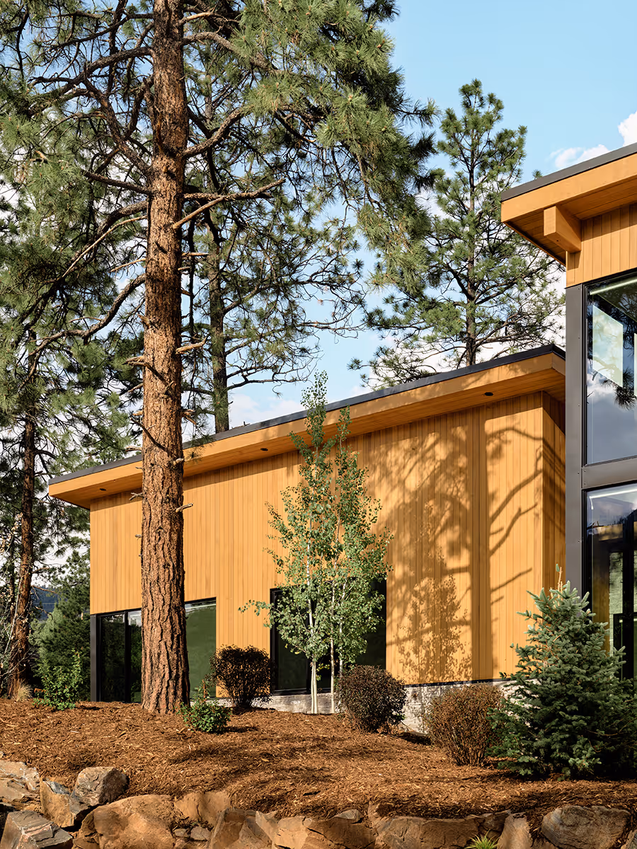 modern mountain home in Durango, Colorado with lots of glass, a stacked stone chimney and wood siding by The Ranch Mine