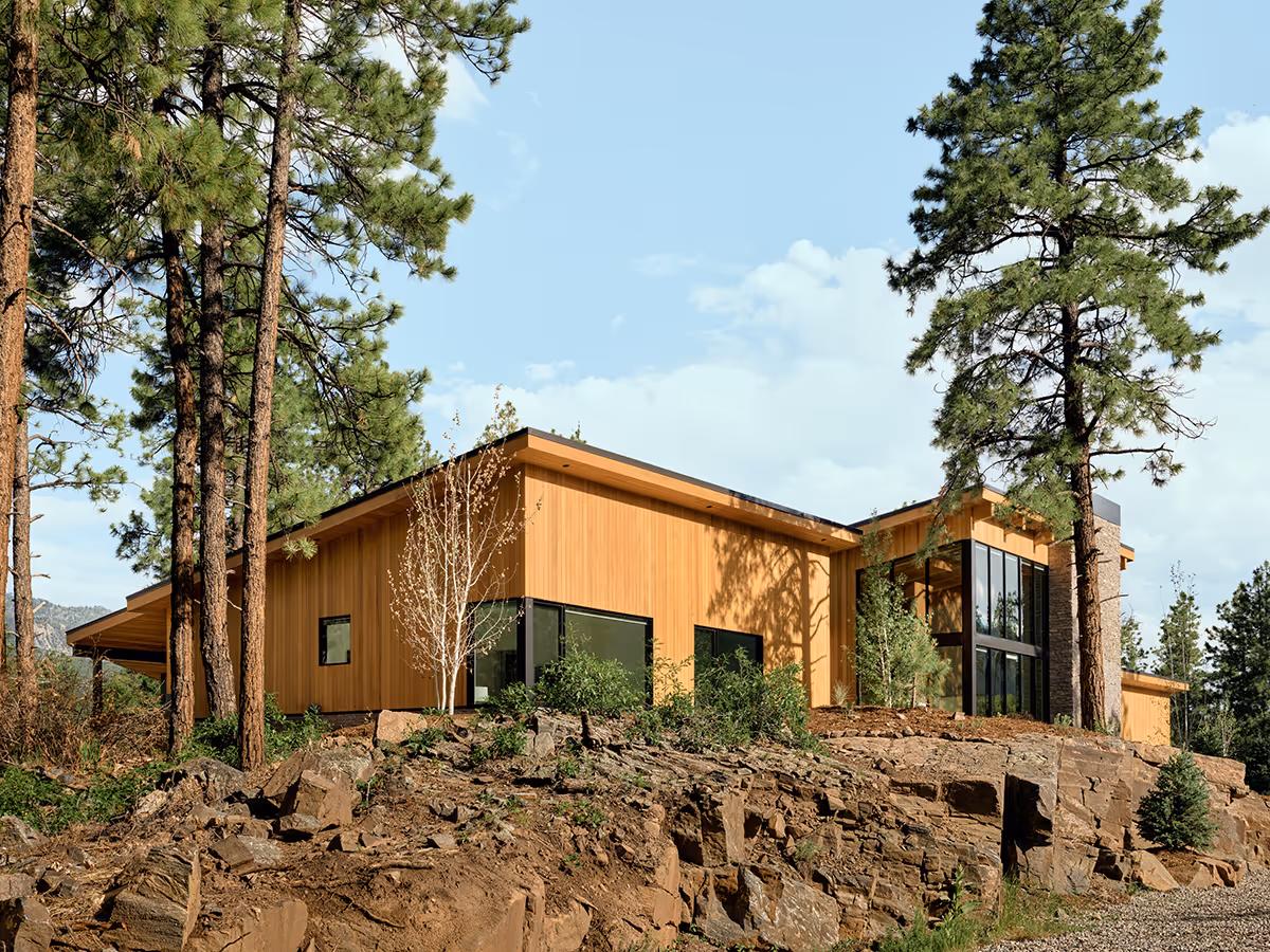 modern mountain home in Durango, Colorado with lots of glass, a stacked stone chimney and wood siding by The Ranch Mine