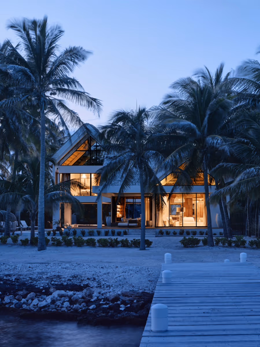 Night time at a concrete tropical modern house with a thatched roof and pool in Belize by The Ranch Mine